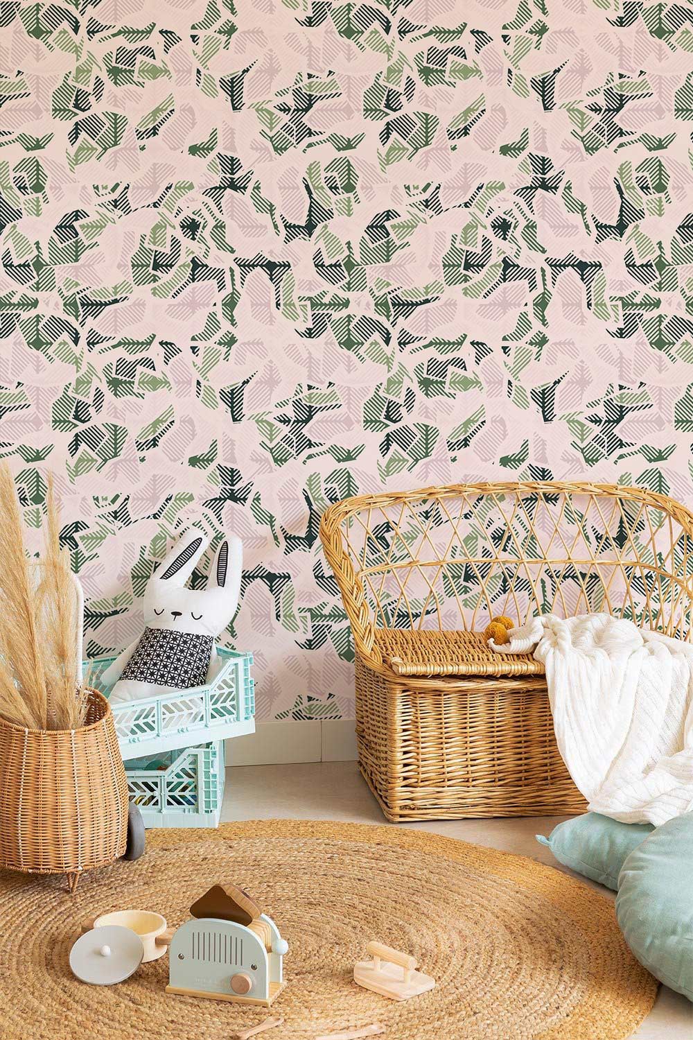 Abstract camouflage wallpaper in nursery with wicker chair, round woven rug, and plush rabbit toy.