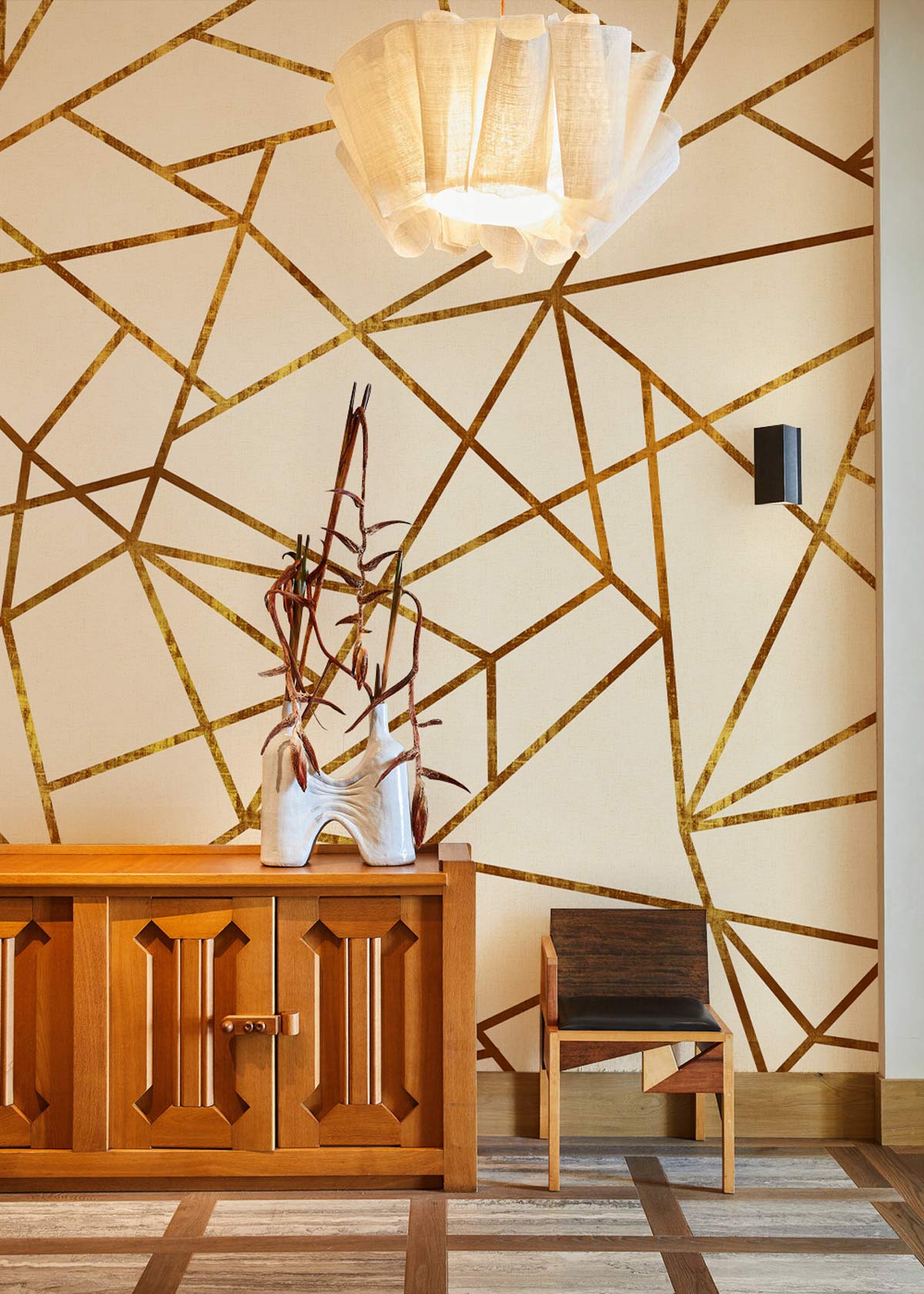 Contemporary gold geometric wallpaper in modern interior featuring wooden cabinet, chair, and pendant light.