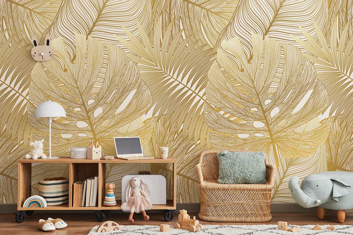 Elegant gold tropical leaf wallpaper in cosy playroom with wicker chair, wooden shelf, and toys.