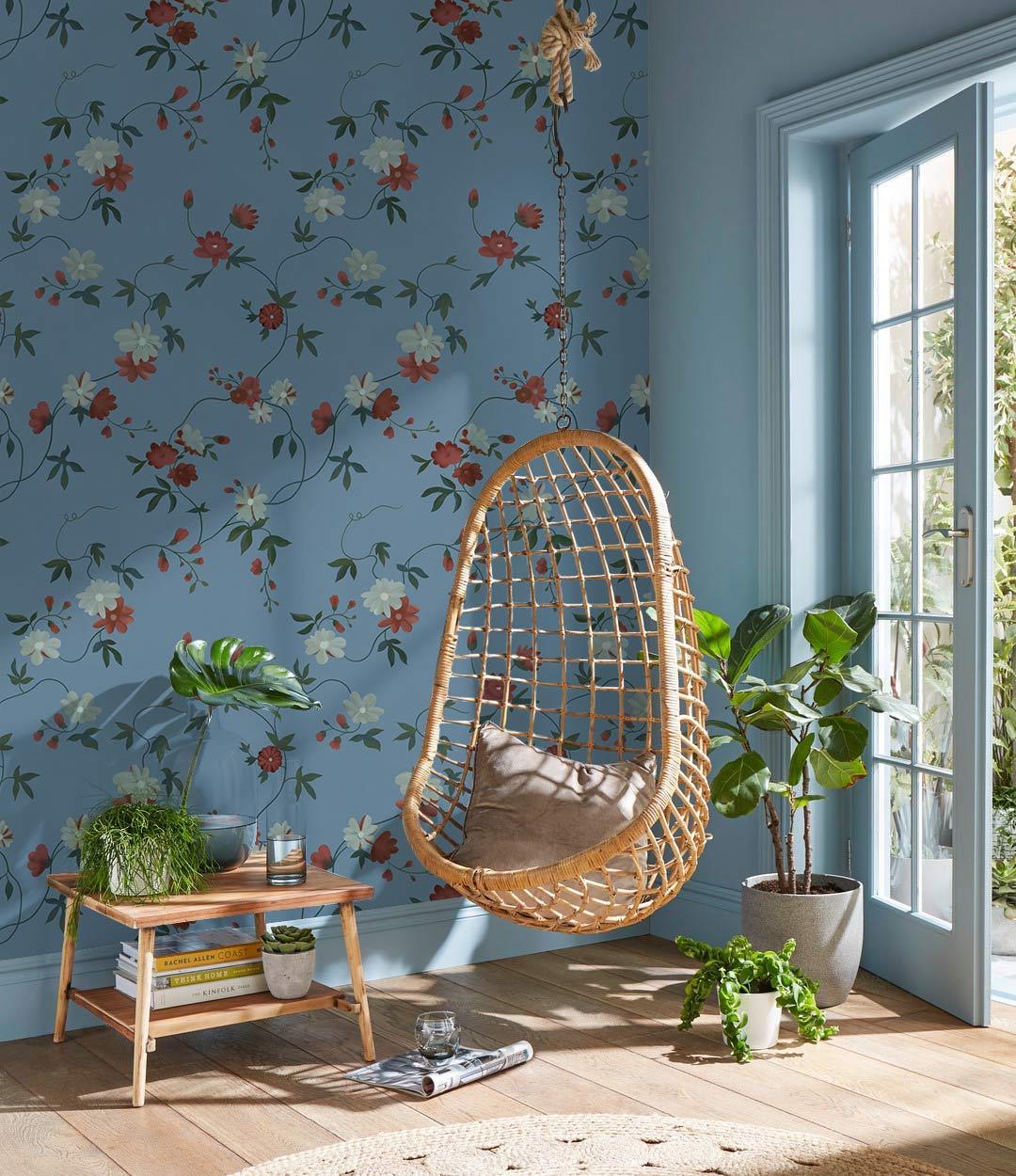 Vintage floral wallpaper with blue and red blossoms, wicker hanging chair, wooden flooring, and plants.