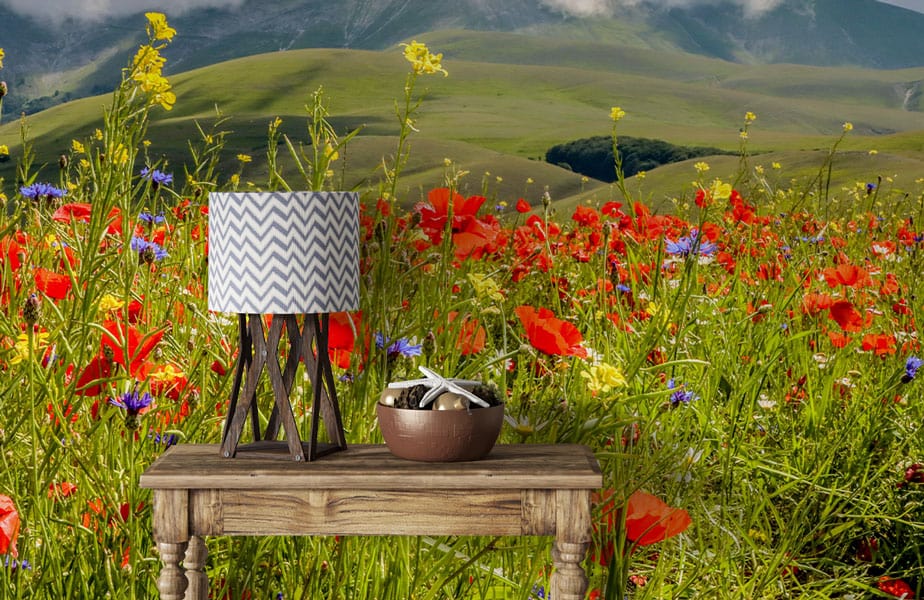 Vibrant Countryside Blossom Mural Wallpaper with red and green design, featuring rustic table and lamp.