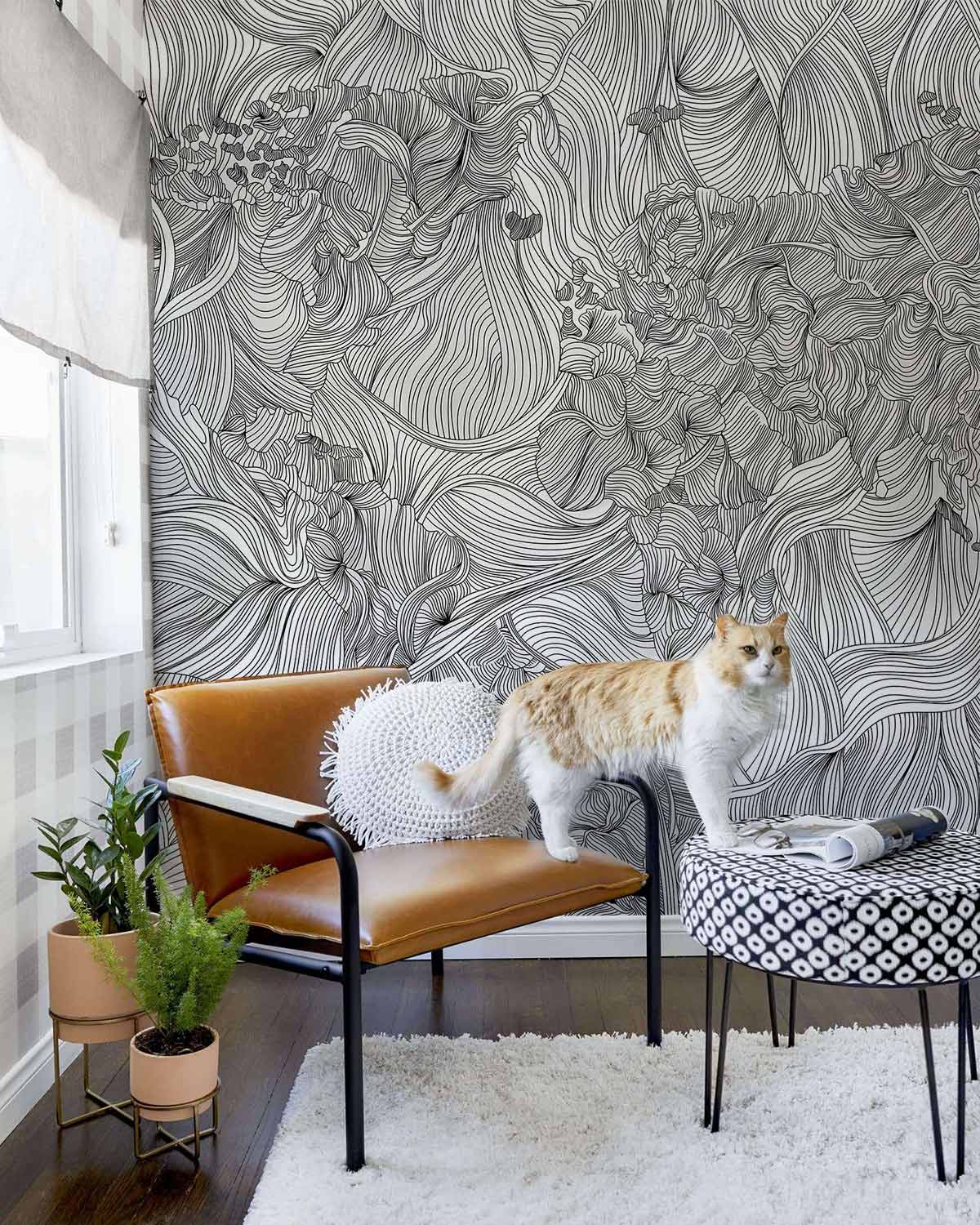 Monochrome Floral Fantasy wallpaper in lounge with brown leather chair, patterned ottoman, white rug.