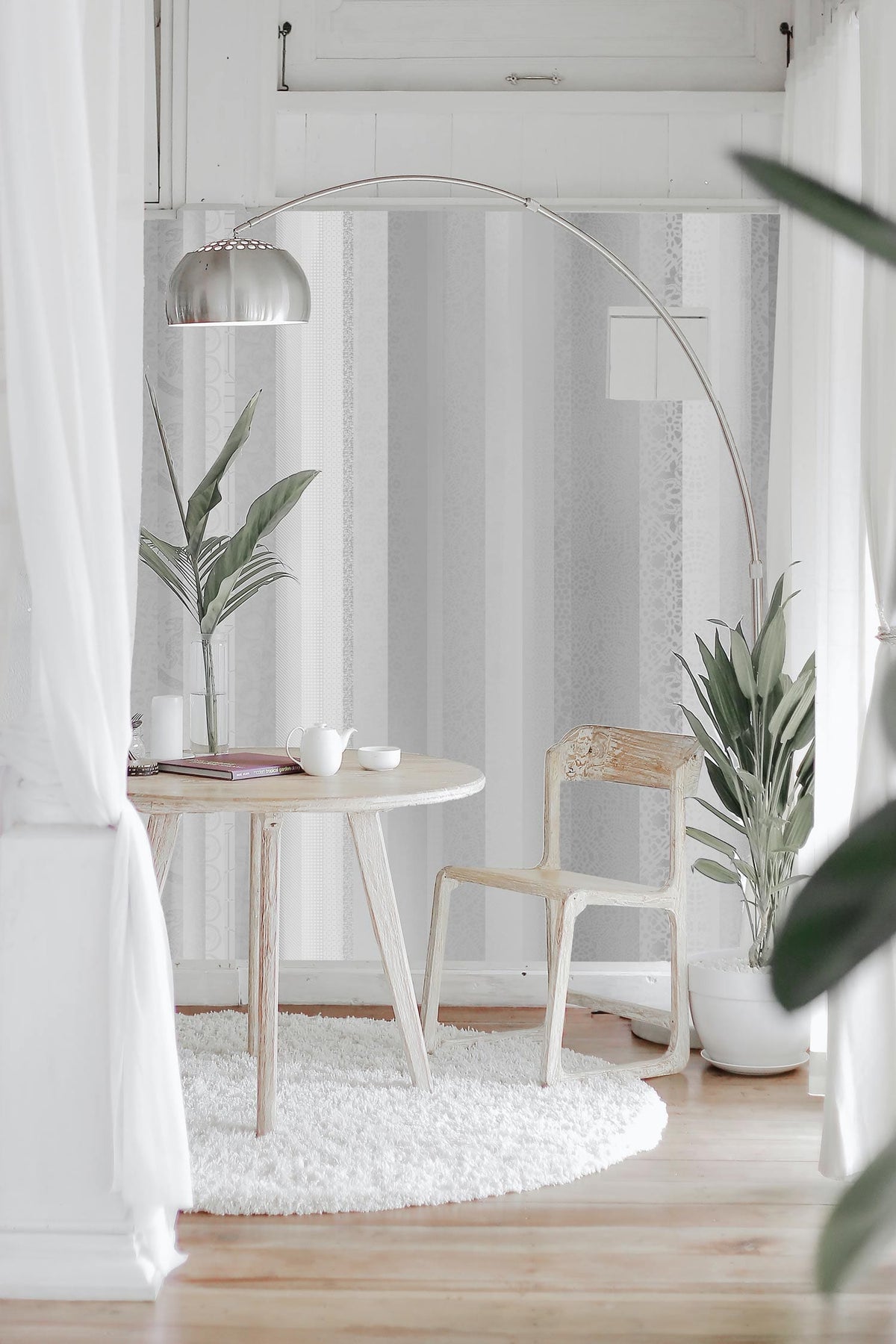 Modern dining nook with wooden chair, round table on white rug, plants, and stylish floor lamp.
