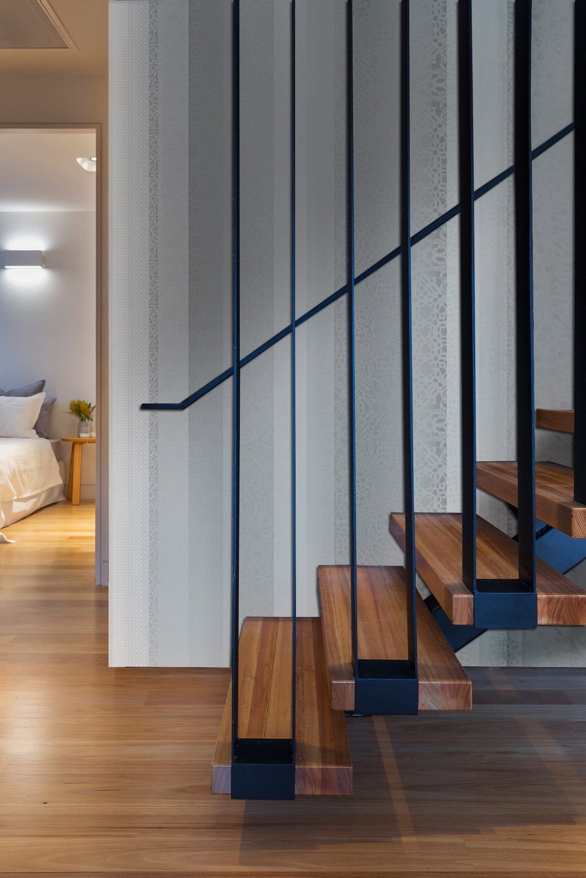 Modern open wooden staircase with black metal railing, light wood flooring, and a glimpse of bedroom.