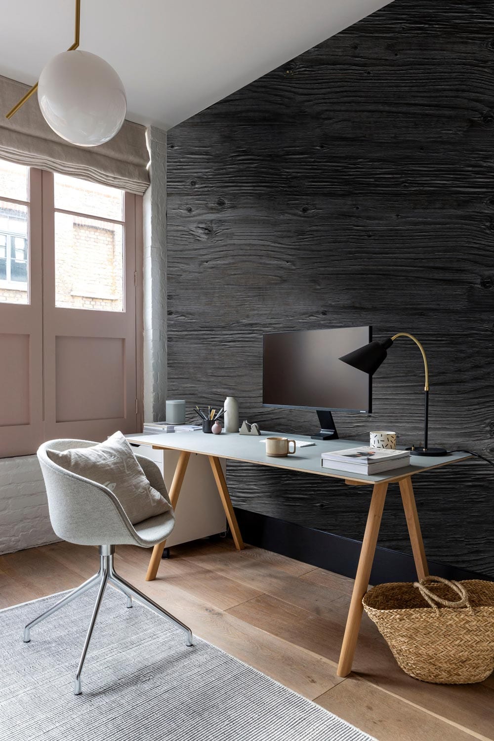 Elegant charcoal grey wood wallpaper in modern home office with minimalist desk, cosy chair, and basket.