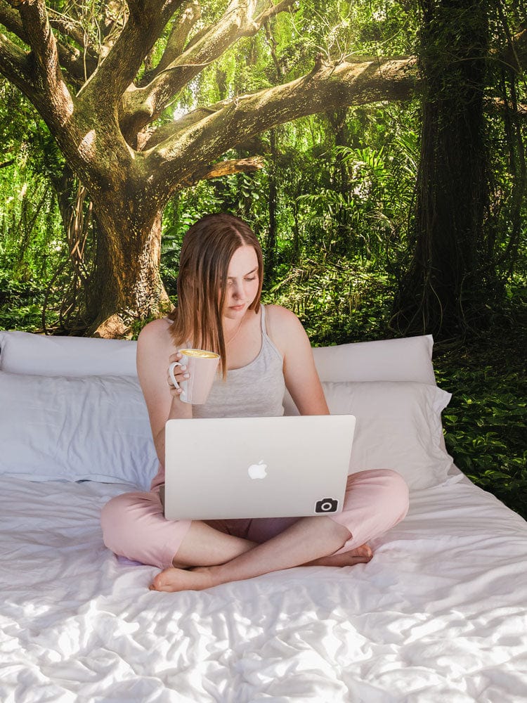 Young woman enjoying tea and working on the laptop in front of forest-themed green tree mural wallpaper.