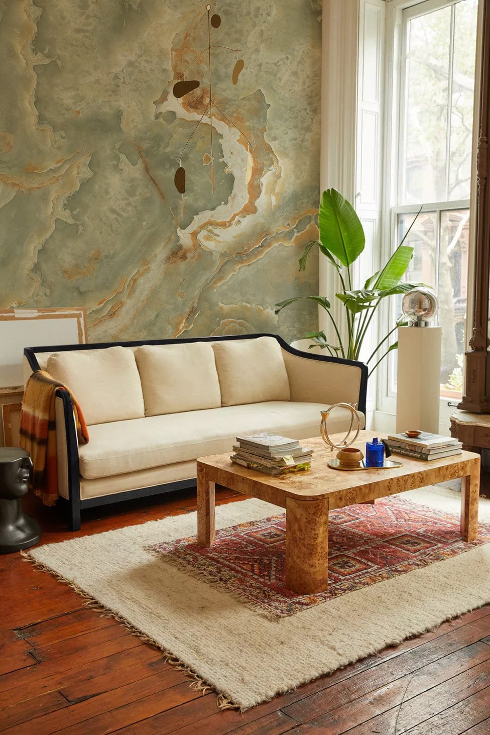 Elegant living room with abstract green marble wallpaper and gold accents, cream sofa, wooden flooring.