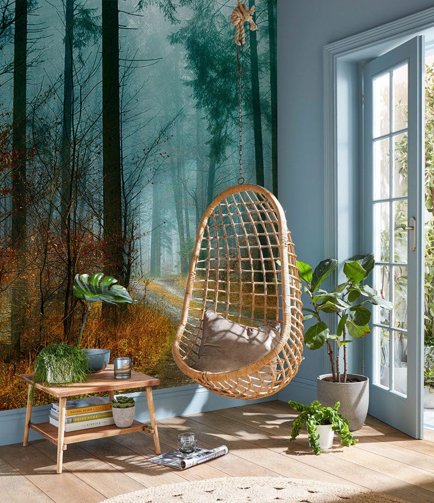 Enchanted misty forest mural wallpaper, hanging wicker chair, wooden flooring, bright elegant living room.