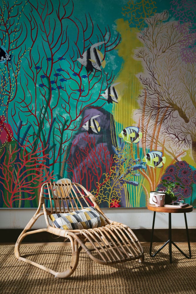 Tropical mural wallpaper with vibrant coral reef, rattan chair, side table, and woven flooring.