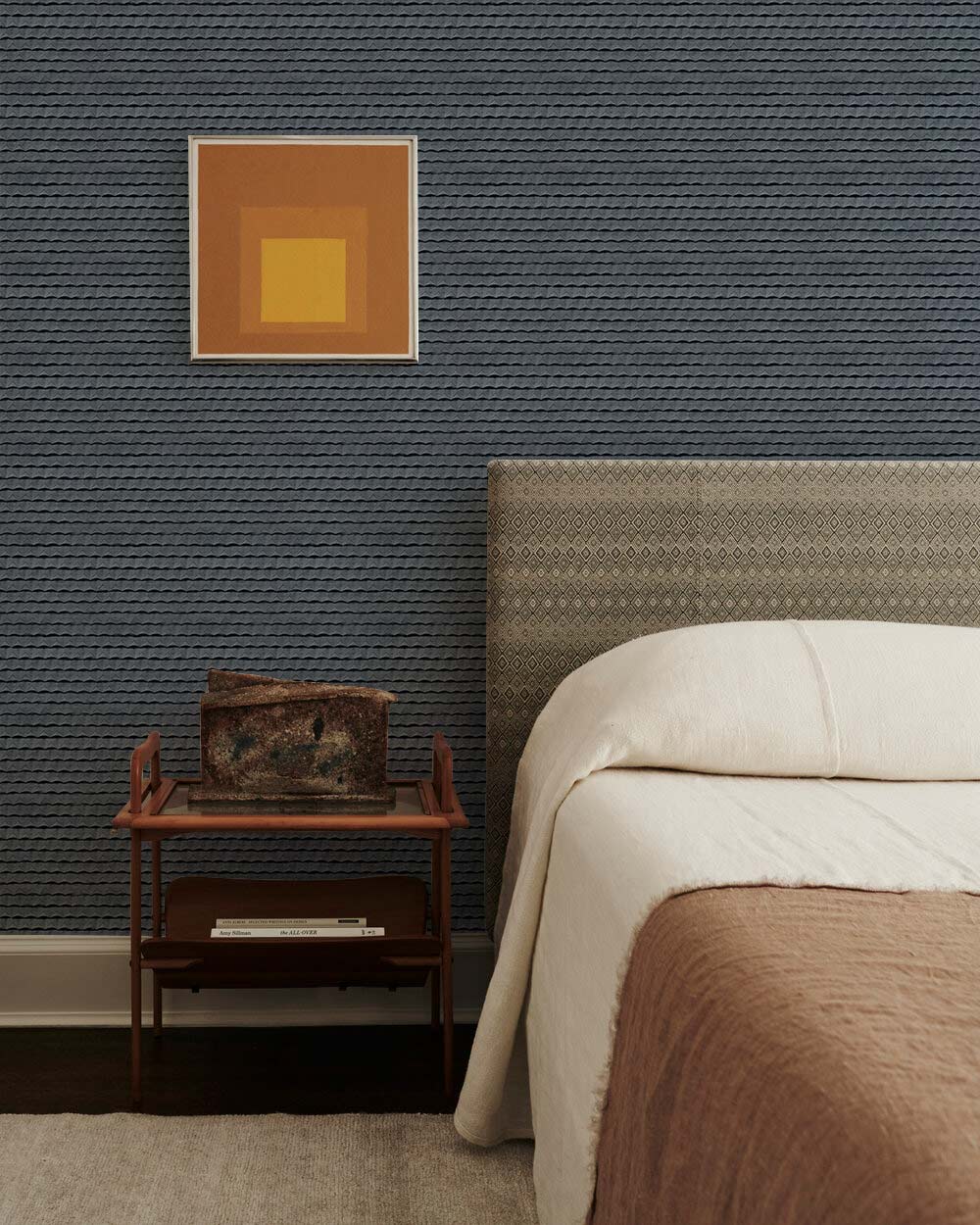 Charcoal grey textured stripe wallpaper in bedroom with beige bedspread, carpet flooring, and abstract art.