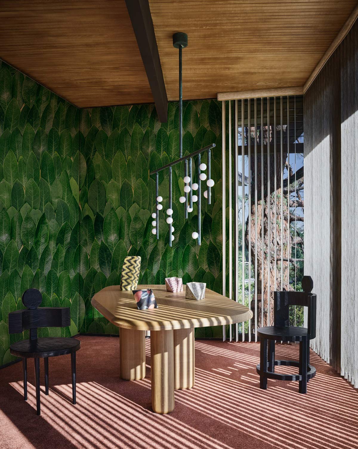 Verdant Leafy Escape wallpaper, botanical pattern, wooden ceiling, modern furniture, black chairs, textile flooring.