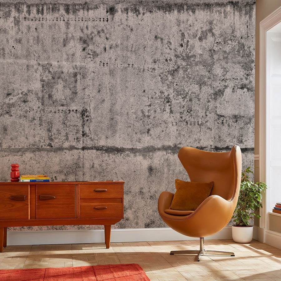 Industrial grey textured wall mural with brown swivel chair, wooden sideboard, beige floor, red rug.