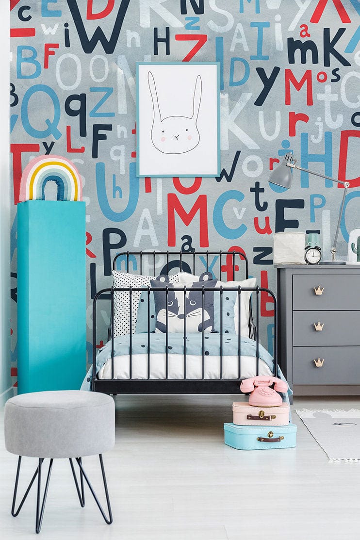 Colourful alphabet wallpaper mural in kids' room with black bed, grey dresser, and blue-red decor.