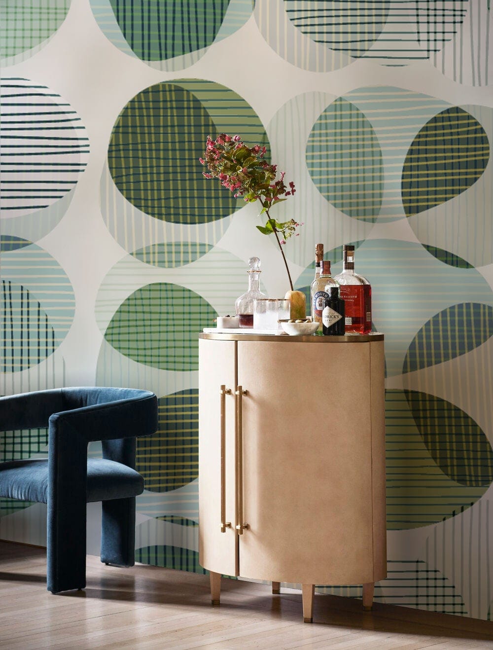 Abstract geometric green circles wallpaper in room with beige cabinet, blue velvet chair, wood flooring.