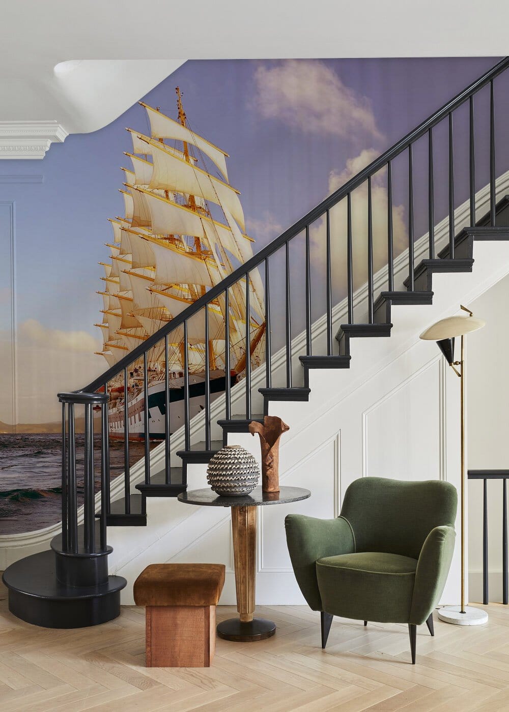 Majestic sailing ship mural enhances nautical Décor, with plush green chair, stylish staircase, wooden flooring.