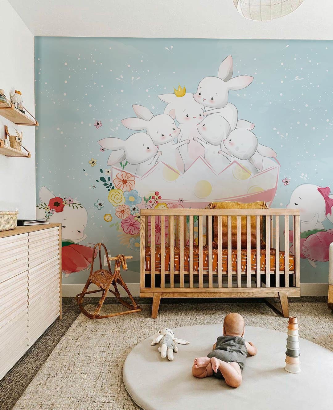 Pastel Spring Bunnies mural wallpaper in nursery with wooden cot, rocking chair, and soft grey rug.