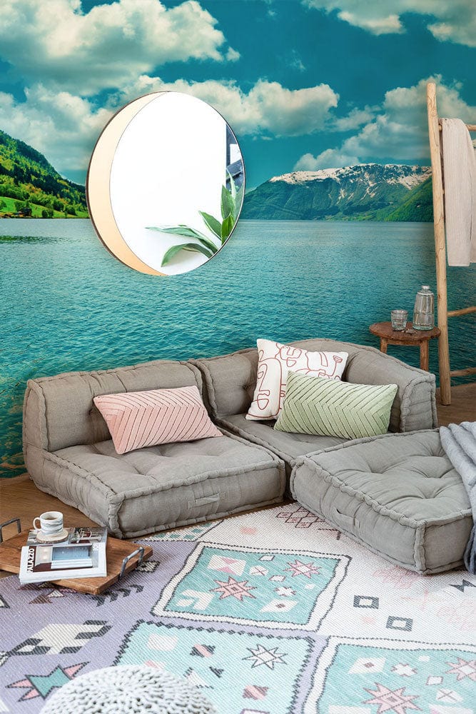 Tranquil mural wallpaper with scenic lake, grey sofa, pastel rug, and round mirror in a living room.