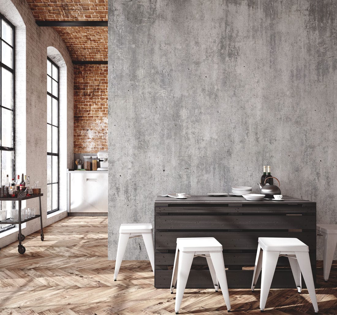 Industrial grey concrete effect mural in modern kitchen; herringbone flooring, brick walls, white stools.