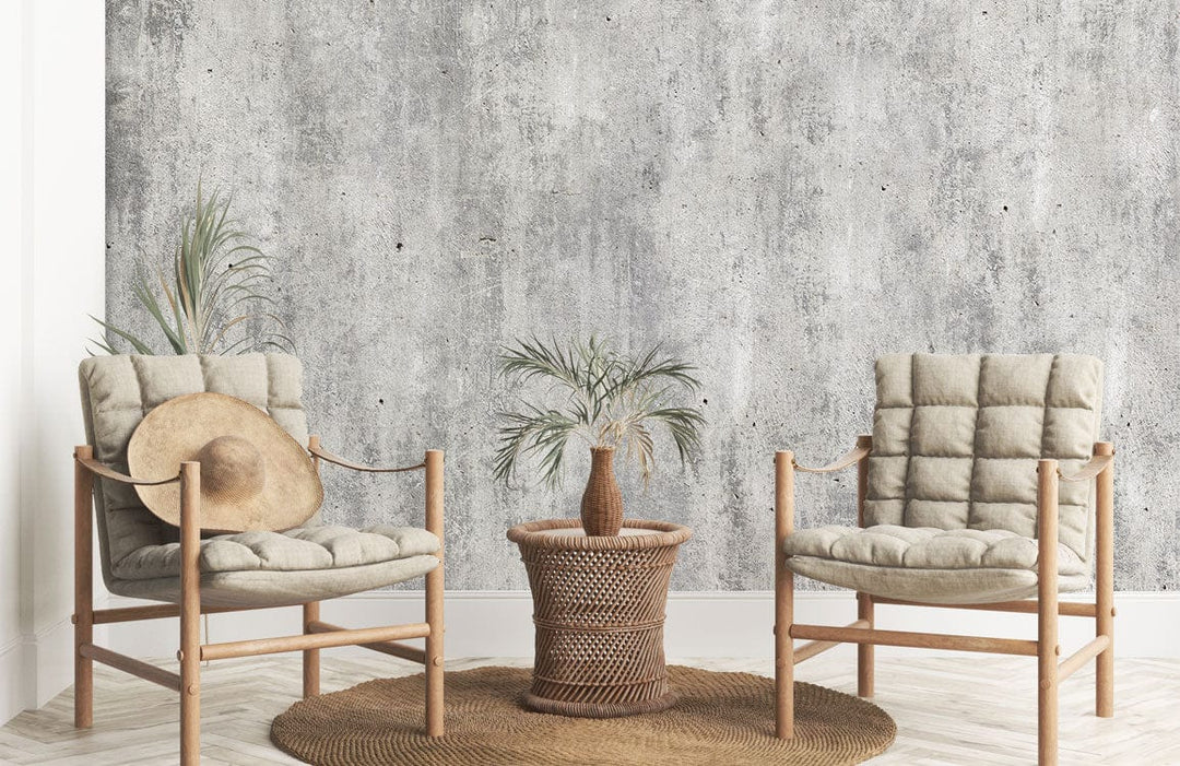Trendy lounge with Industrial Grey Concrete Effect Mural Wallpaper, beige cushioned chairs, wicker table, rug.
