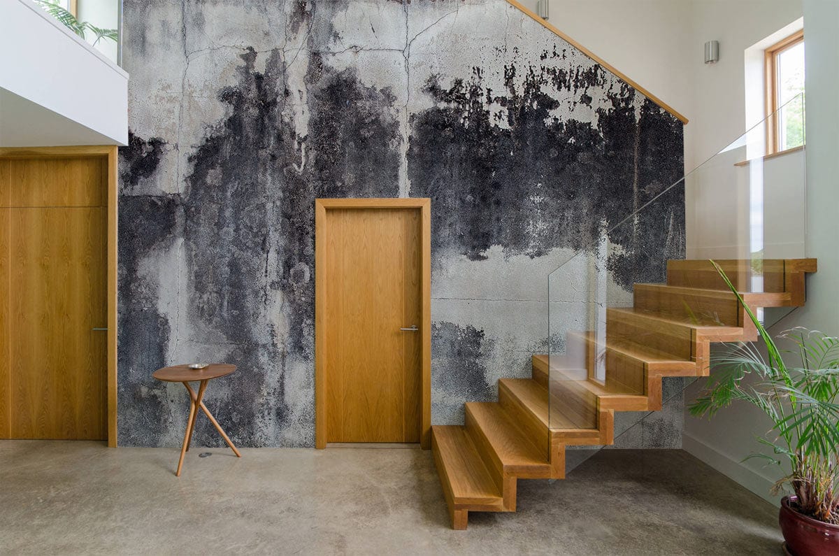 Alt text: Vintage industrial concrete wall mural in hallway with wooden staircase and neutral flooring.