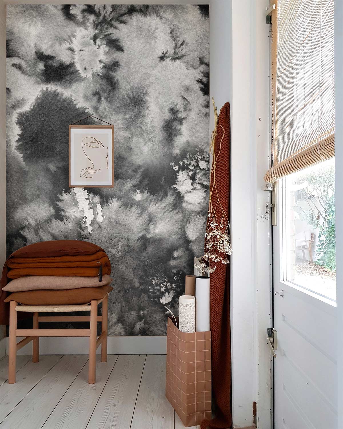 Monochrome watercolour cloudburst mural wallpaper in grey with wooden chair, minimal artwork, light wood flooring.