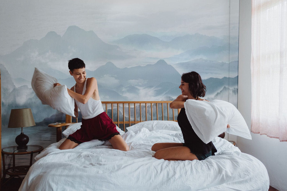 Ethereal Misty Mountains wallpaper, wooden bed, white bedding, soft light, tranquil bedroom setting.