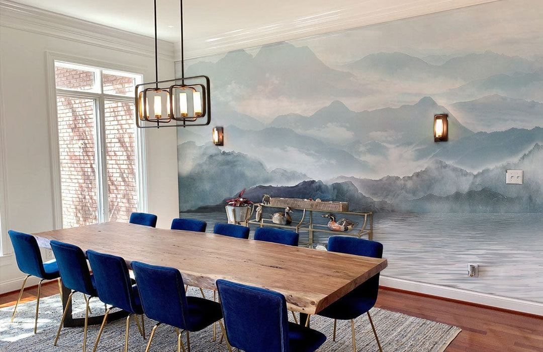 Ethereal Misty Mountains wallpaper, dining room, oak table, blue chairs, modern chandelier, wooden flooring.