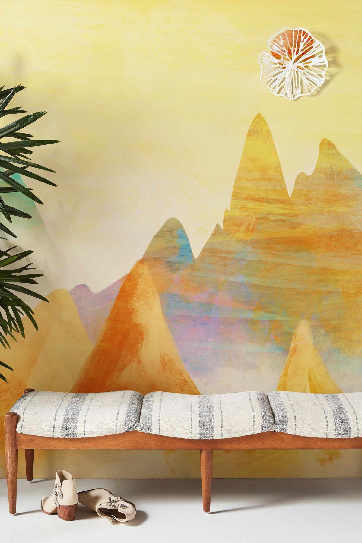 Dreamy mountain mural wallpaper with warm pastels, mid-century bench, wooden flooring, and bohemian decor.