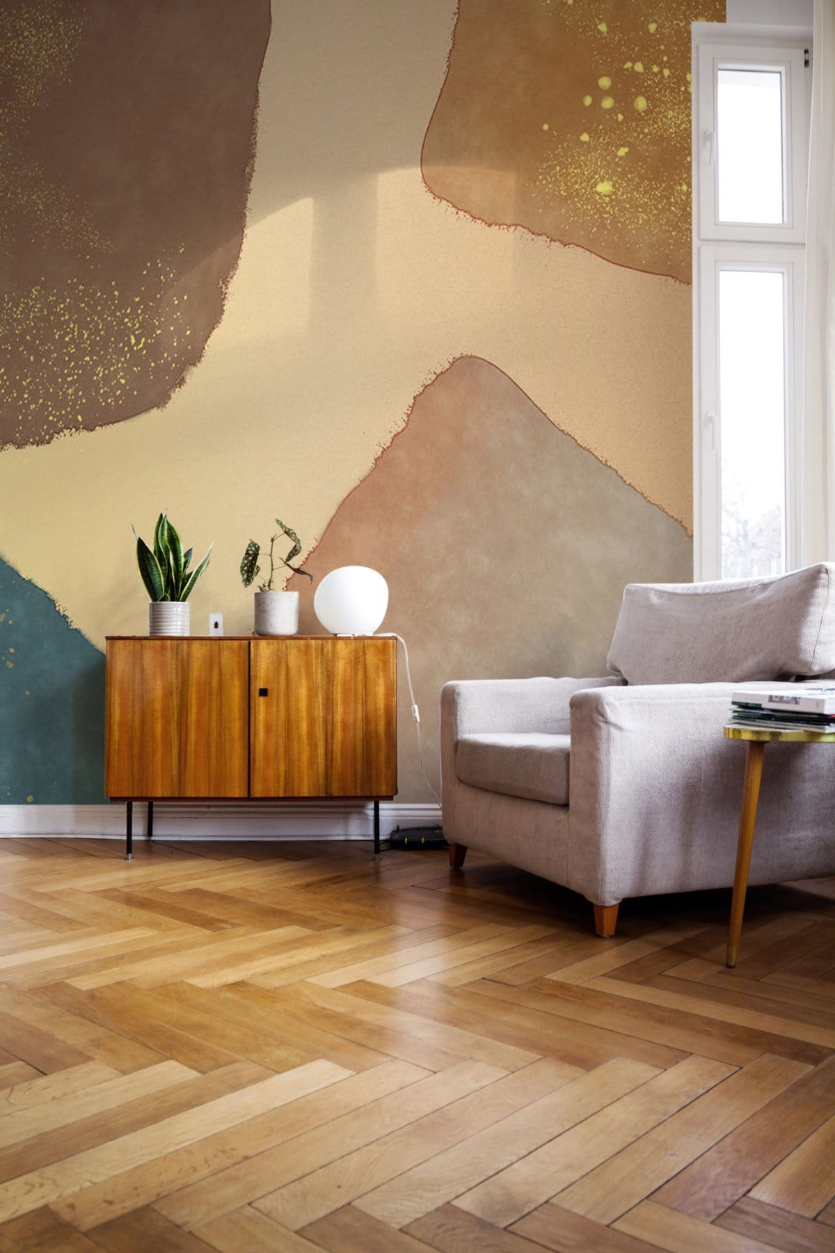 Rustic mural wallpaper, beige and teal, mid-century modern armchair, wooden sideboard, herringbone floor.