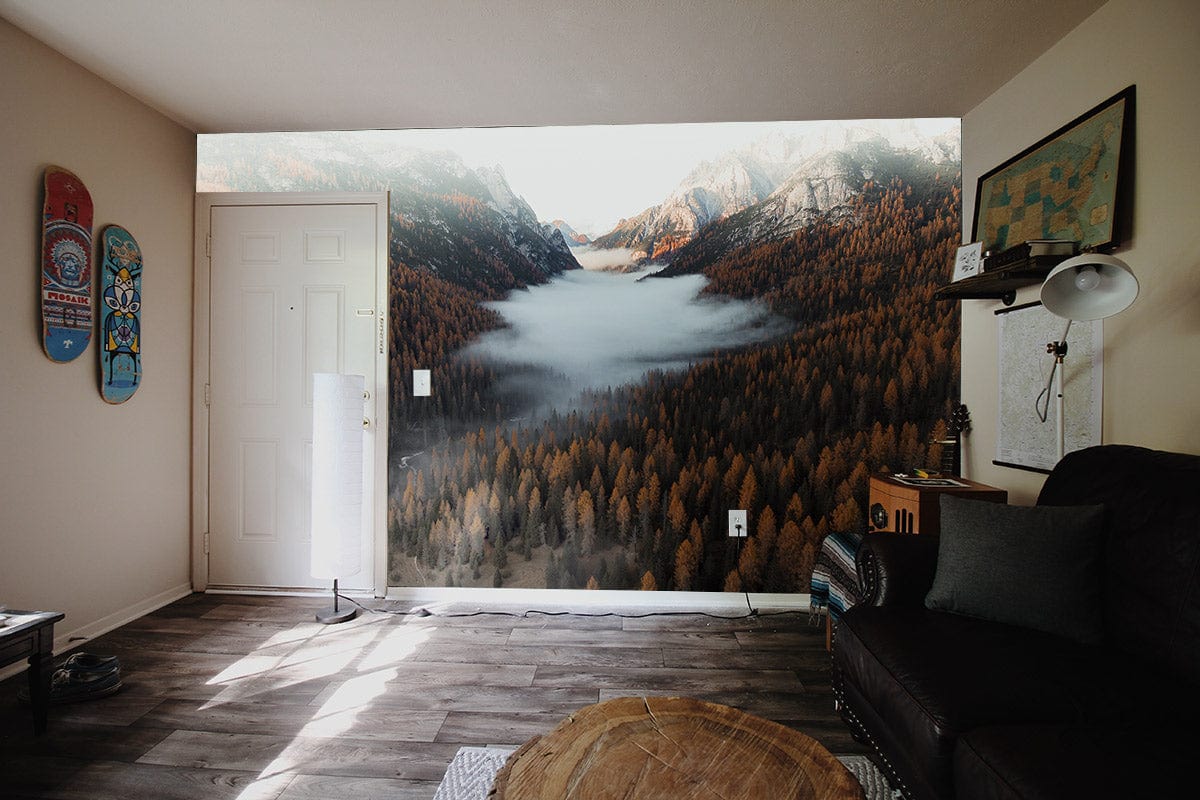 Majestic Alpine Forest mural wallpaper, misty mountain views, autumn hues. Living room, dark sofa, wooden flooring.