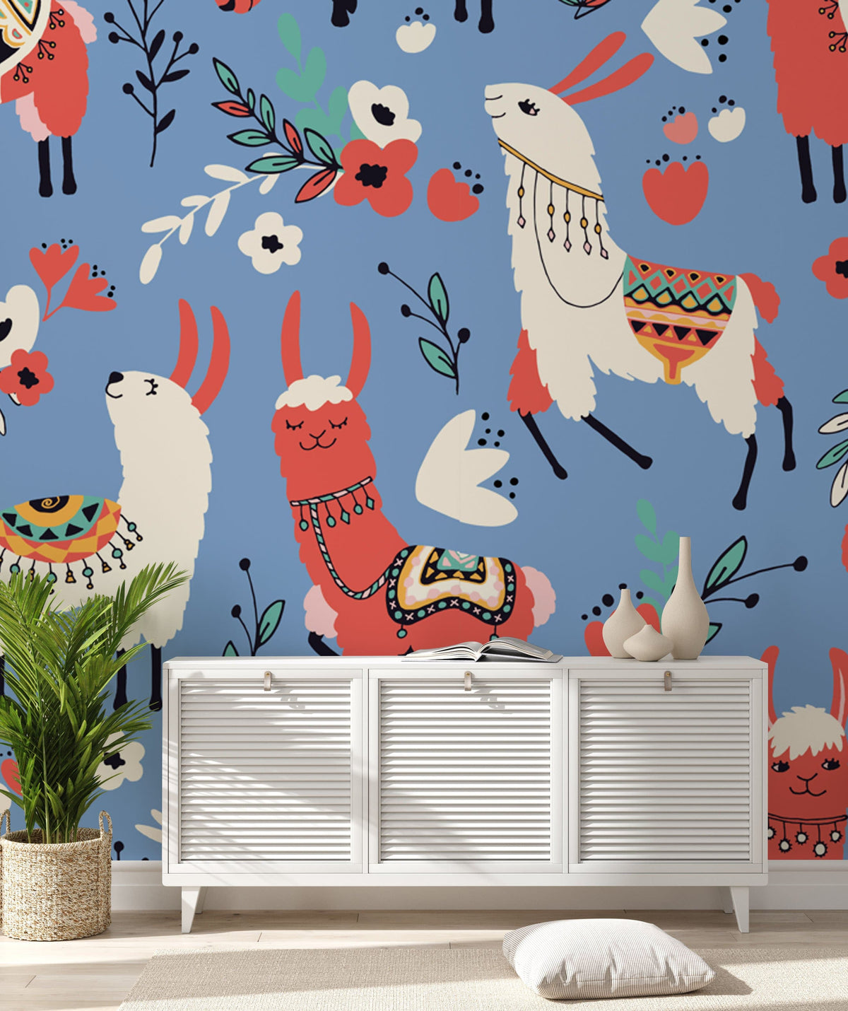Whimsical llama pattern wallpaper, blue background, vibrant red, white. White sideboard, wooden flooring, potted plant.