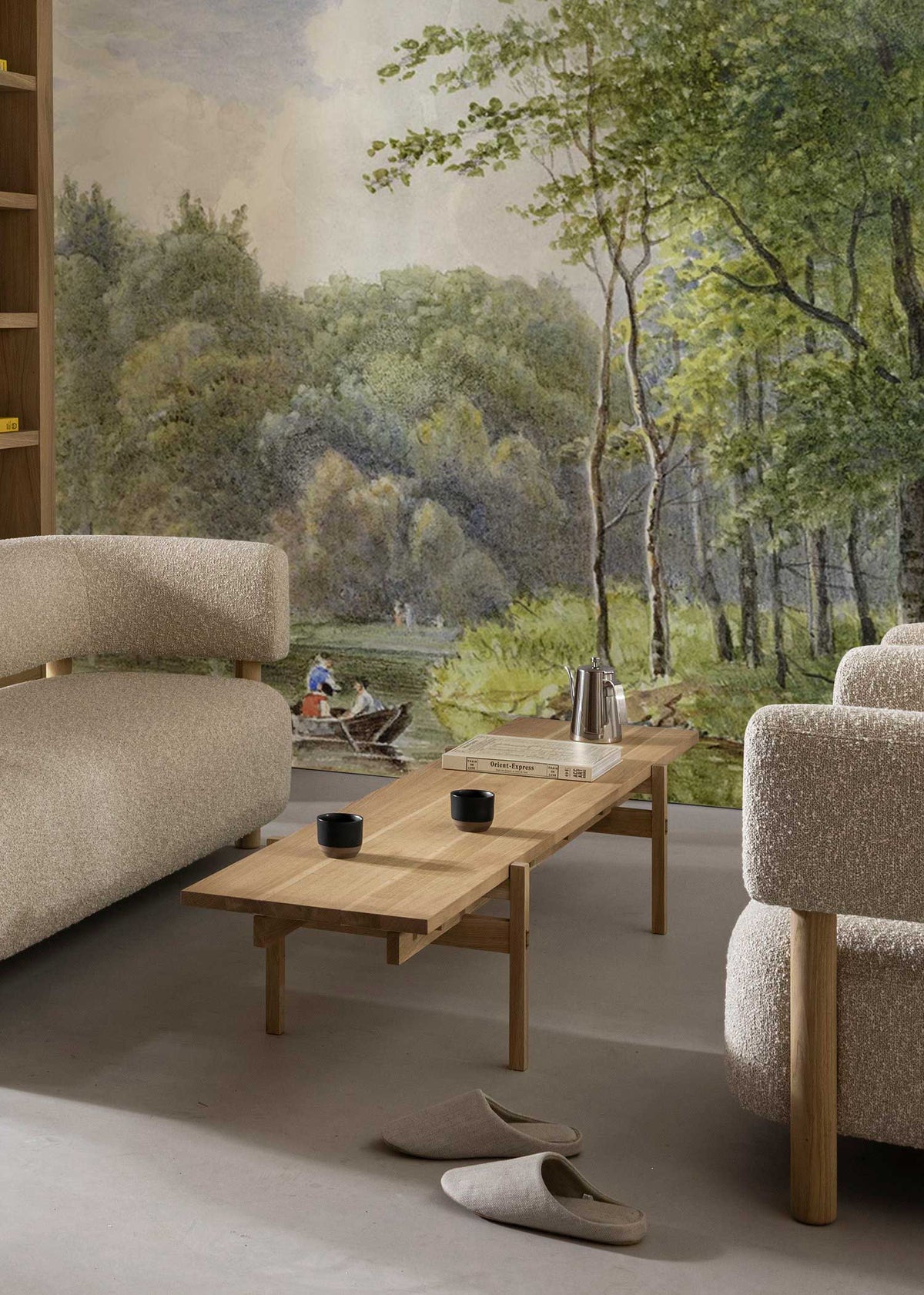 Tranquil riverside mural wallpaper in lounge with beige sofas and wooden coffee table, forest scene.