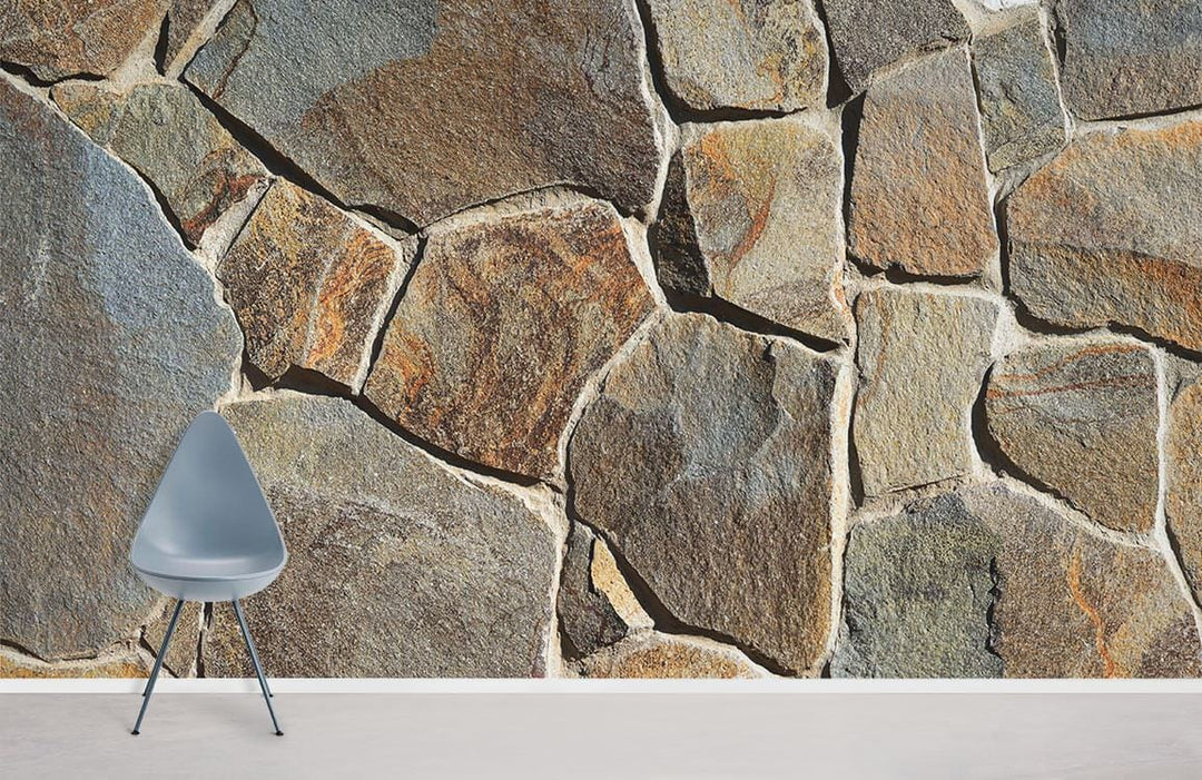 Rustic stone wall mural wallpaper with natural earth tones, featuring modern grey chair on white floor.