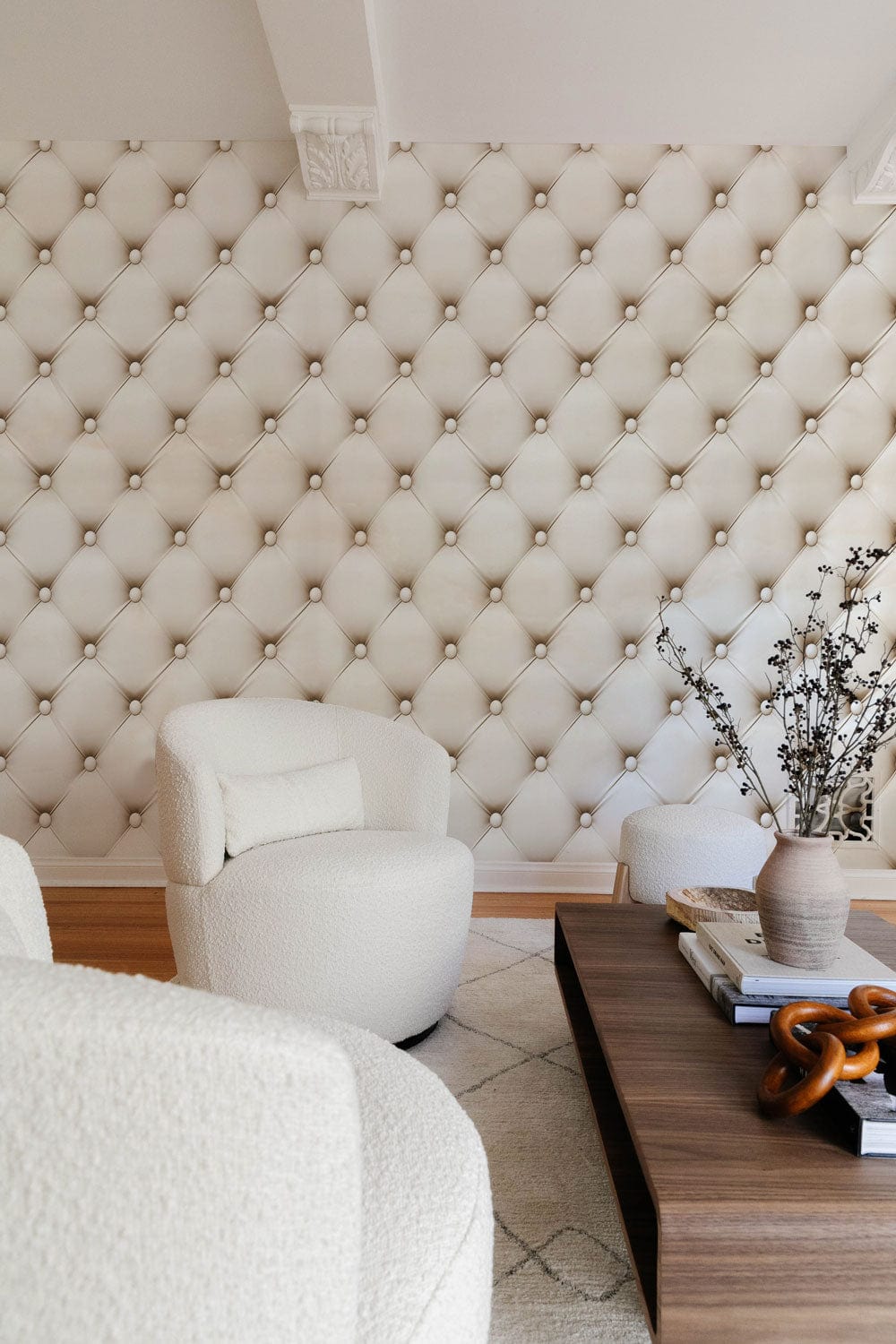 Luxurious cream quilted wallpaper, elegant lounge setting with plush armchairs, wooden coffee table.