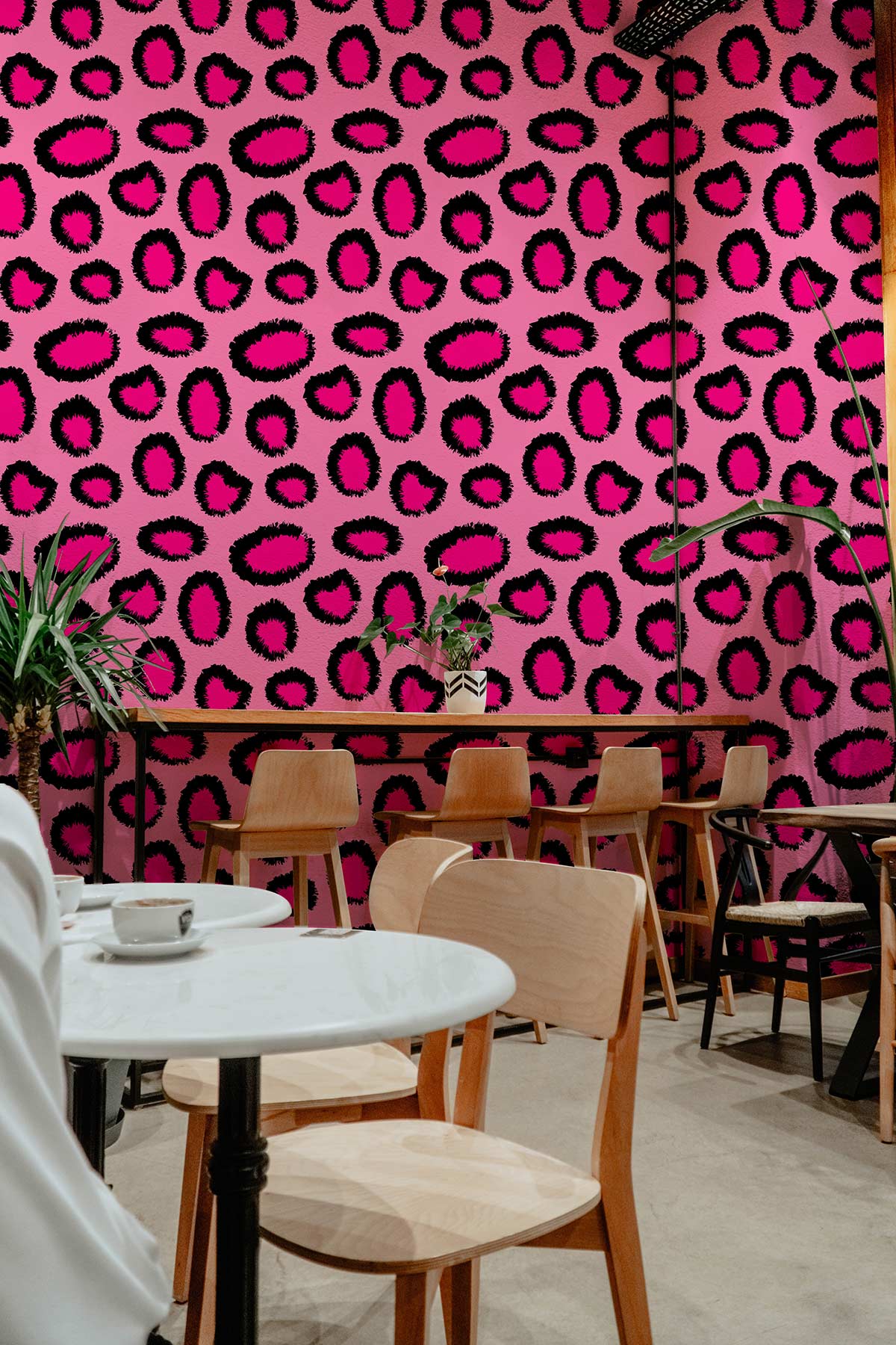 Tropical Pink Leopard Print Wallpaper in modern café setting with wooden chairs and tables.