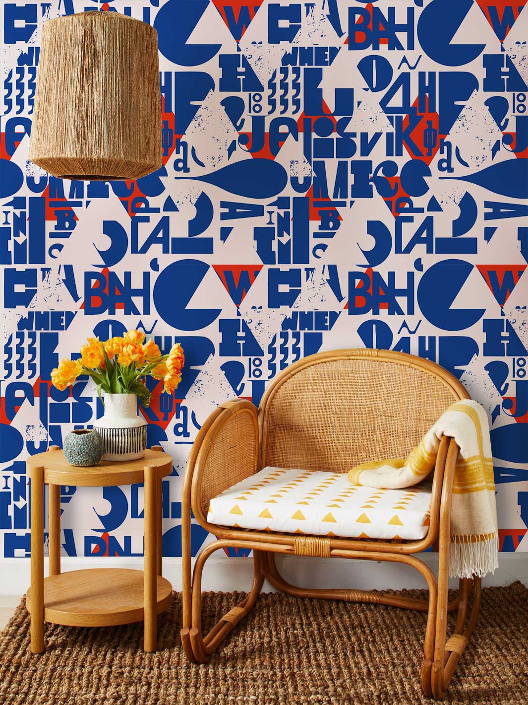 Contemporary blue and red geometric mural wallpaper with rattan chair, woven lamp, and wooden side table.
