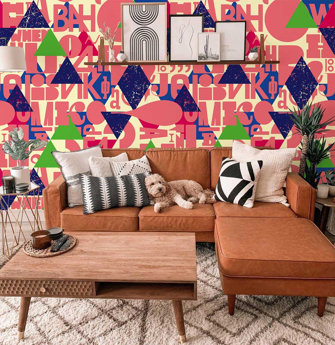 Vibrant retro geometric wallpaper with bold typography behind brown leather sofa in modern living room.