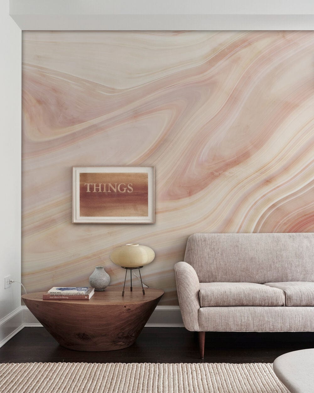 Blush Pink Marble Swirl Mural Wallpaper, beige sofa, dark wood table, modern living room setting.