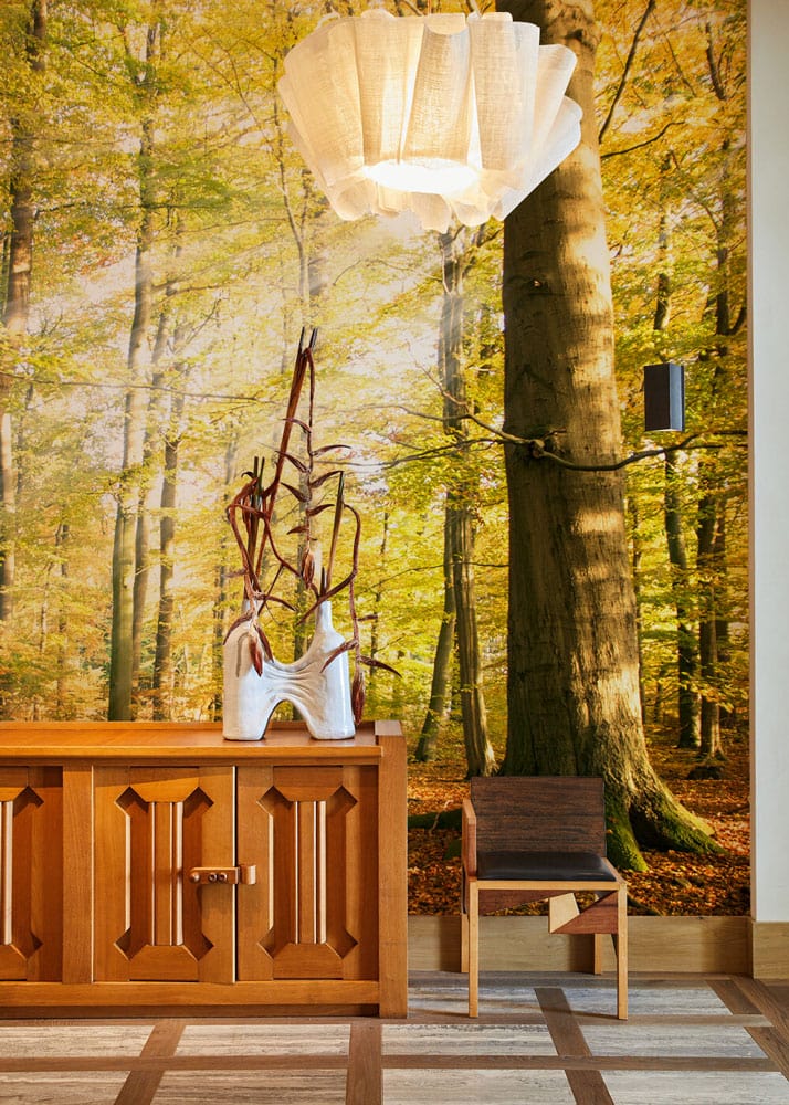 Golden Autumn Mural Wallpaper with wooden chair, sideboard, and pendant light in cosy living room.