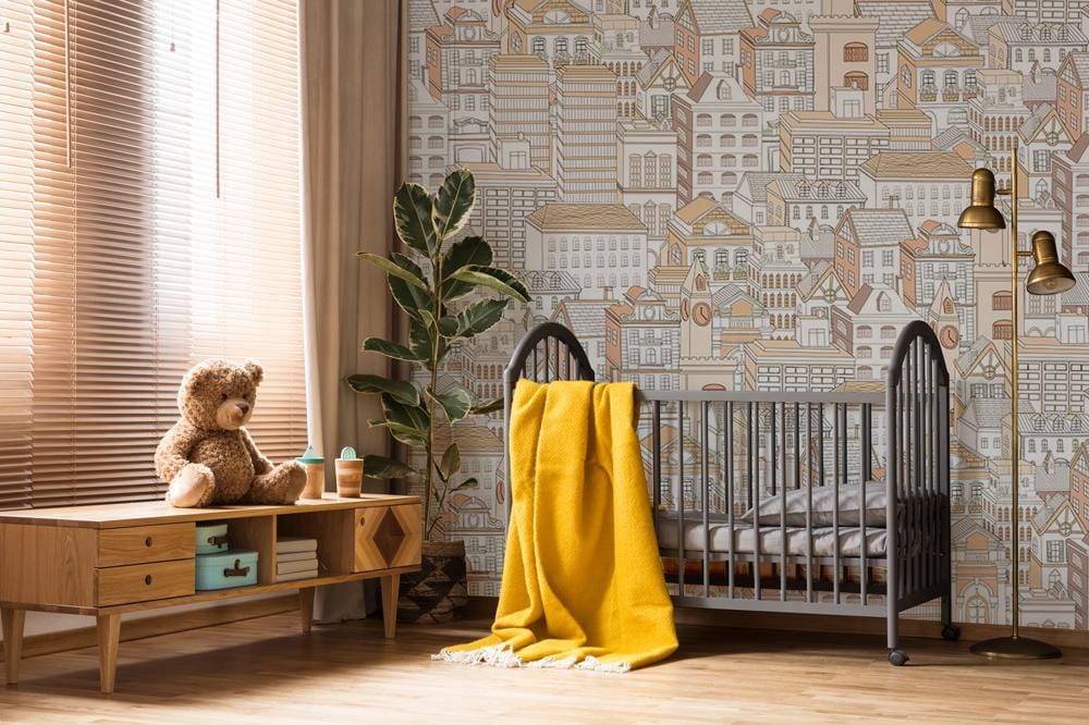 Vintage urban cityscape wallpaper in nursery with wooden flooring, grey crib, and yellow blanket.