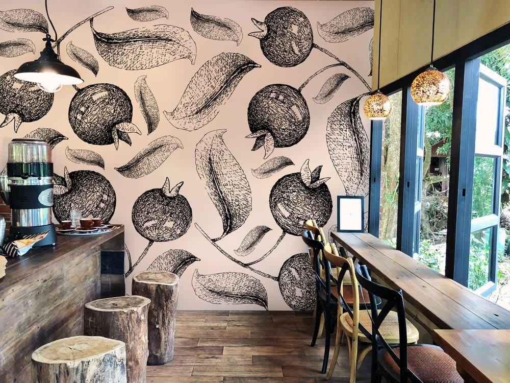 Monochrome pomegranate sketch wallpaper in rustic café with wooden stools, tables, and pendant lights.