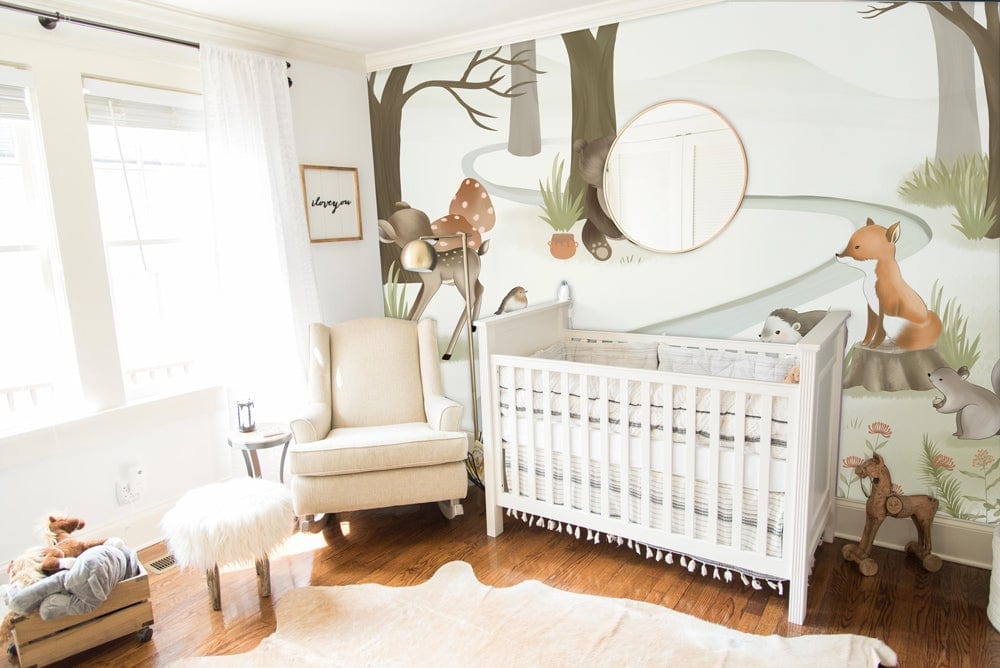 Nursery featuring Woodland Animals Mural Wallpaper, white cot, beige armchair, wooden floor, round mirror.