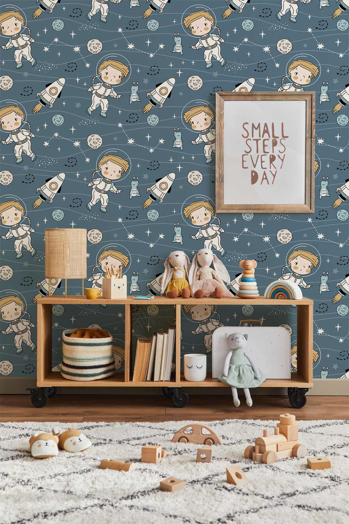 Blue outer space children's wallpaper with astronaut theme in kids' room, featuring playful decor and toys.