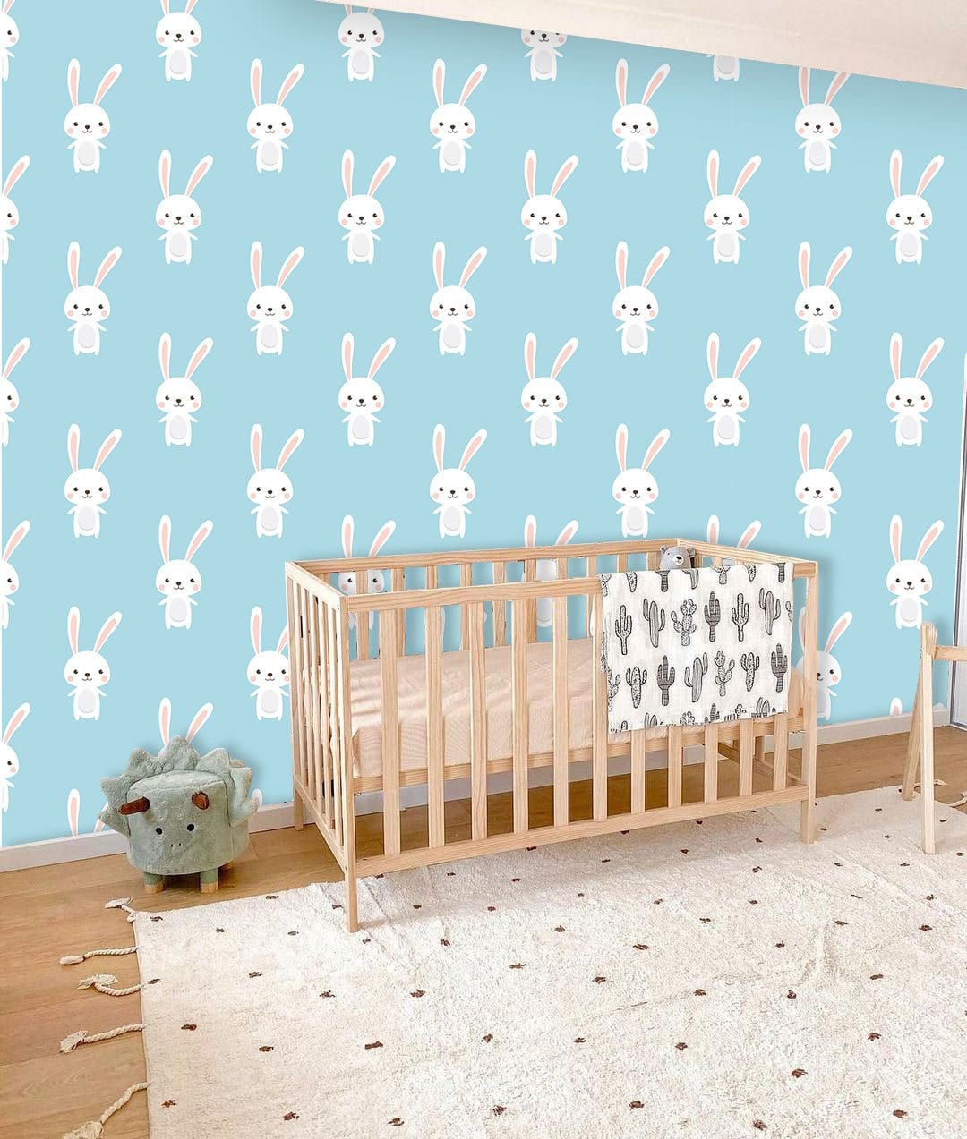 Charming Pastel Blue Bunny Wallpaper in nursery with wooden crib, plush toy, and light wood flooring.