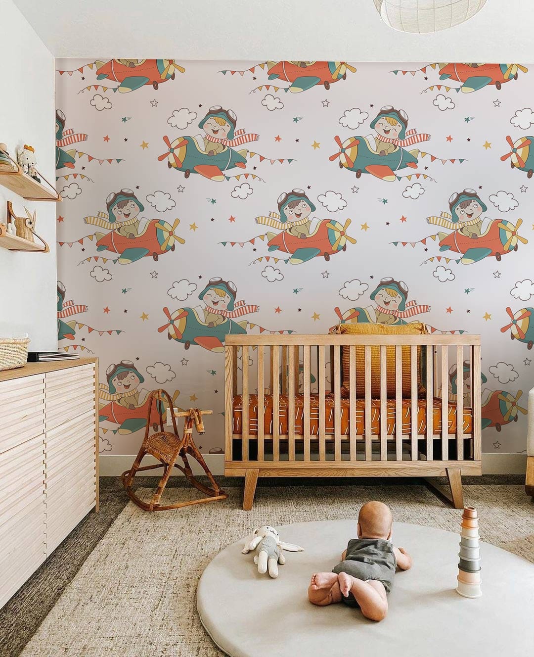 Playful Vintage Aviator Kids' Mural Wallpaper with wooden crib, soft rug, and rocking chair in nursery.