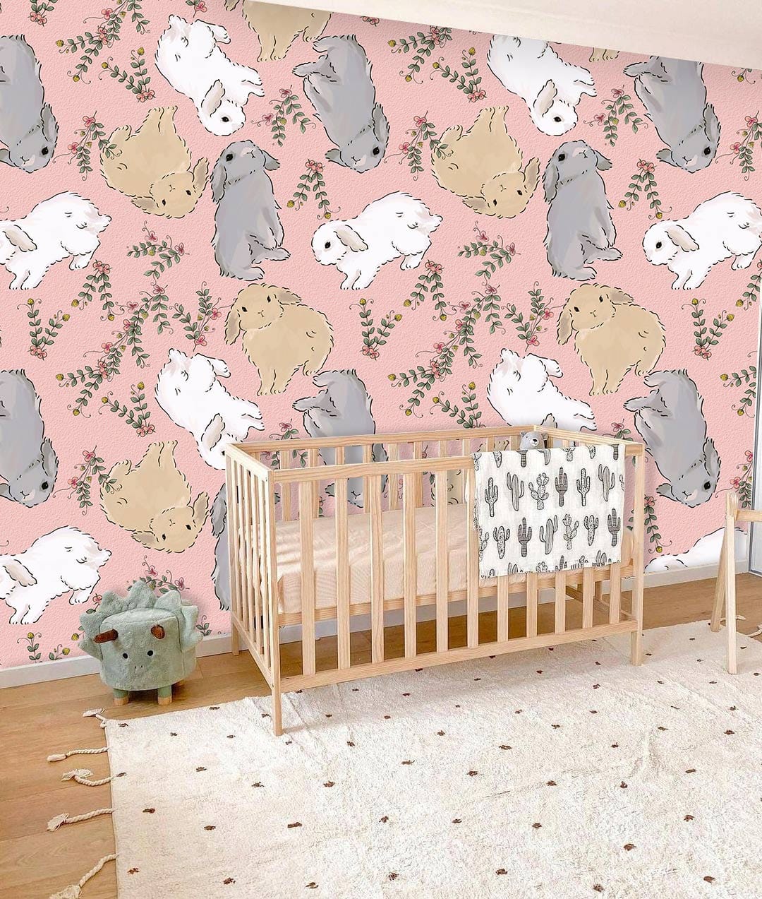 Charming pastel bunny wallpaper in a nursery with wooden crib, pink walls, and cosy white rug.