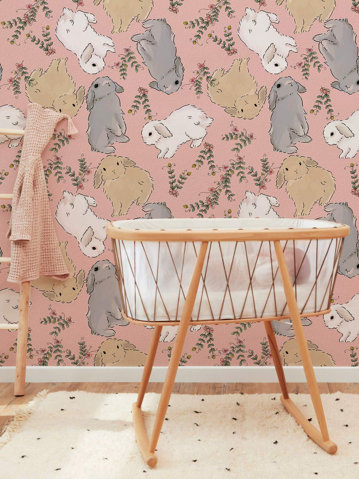 Pastel bunny wallpaper in a nursery, featuring a wooden crib, ladder, and speckled rug.