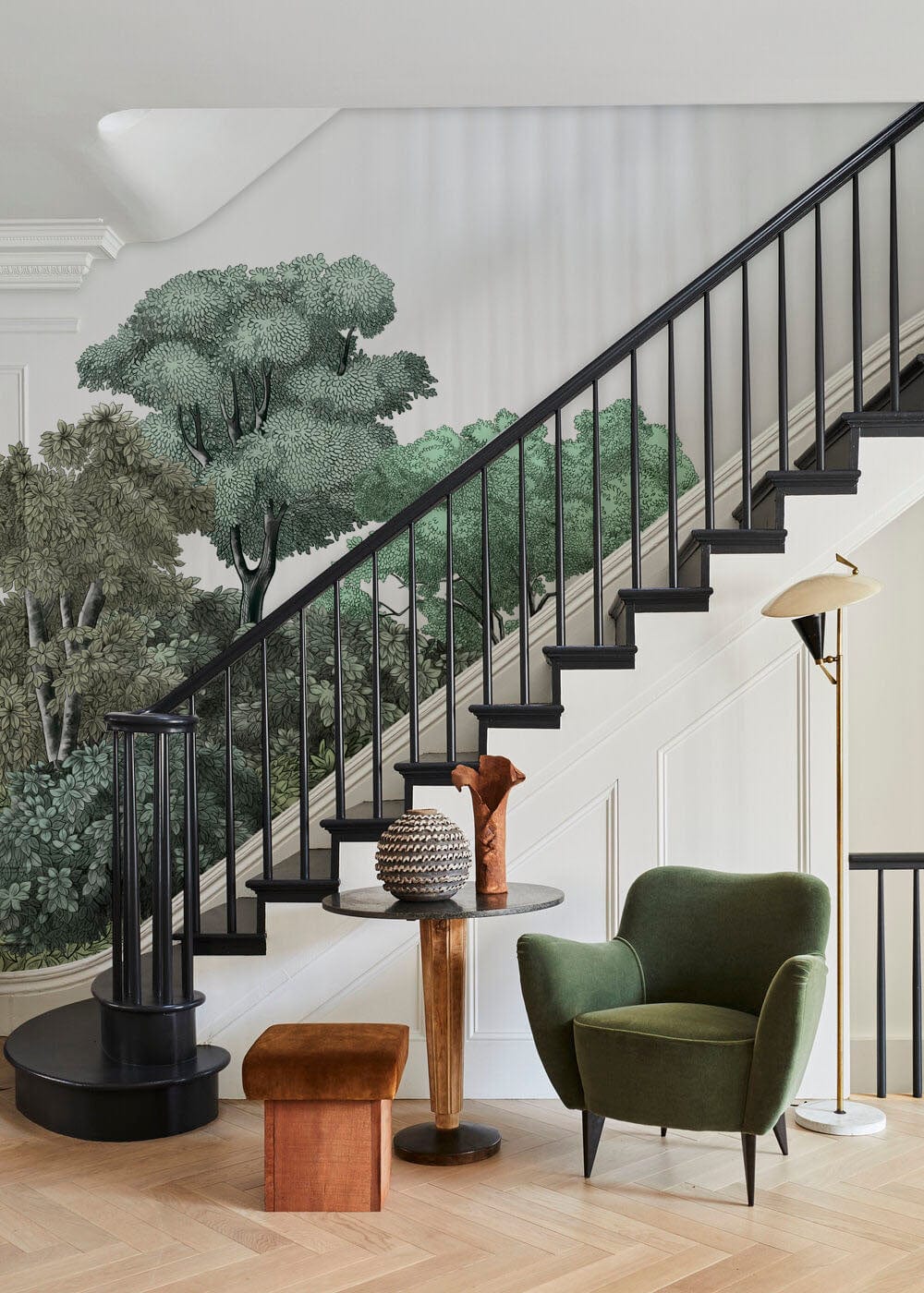Staircase with Serene Forest Green Canopy Mural, green chair, wooden table, and stylish lamp.
