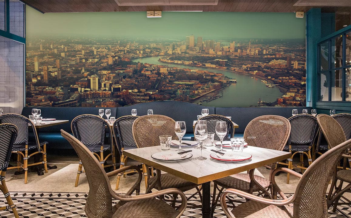London Skyline mural in soft sunset hues in restaurant with woven chairs and wooden tables.