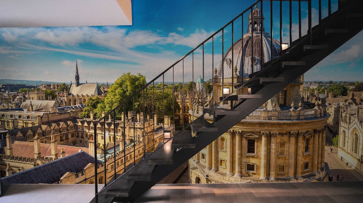 Oxford Skyline Mural Wallpaper featuring classic architecture; modern staircase; light wooden flooring in living room.